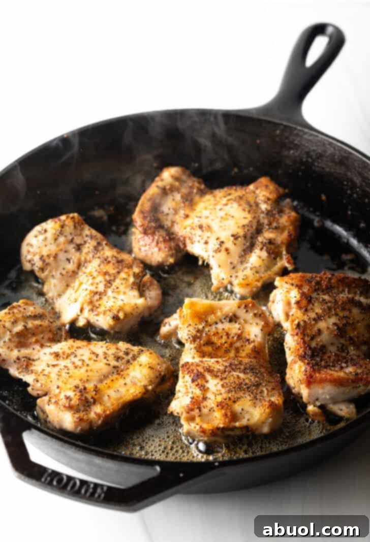 Five perfectly cooked, golden-brown chicken thighs resting in a cast iron skillet, ready to be removed.