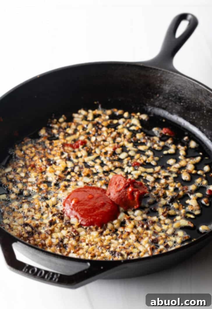 Minced garlic and rich tomato paste sizzling in a cast iron skillet, creating aromatic foundations for the sauce.