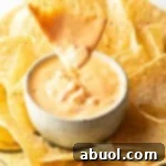 Hand dipping a chip into a white bowl of velveeta cheese dip surrounded by tortilla chips.