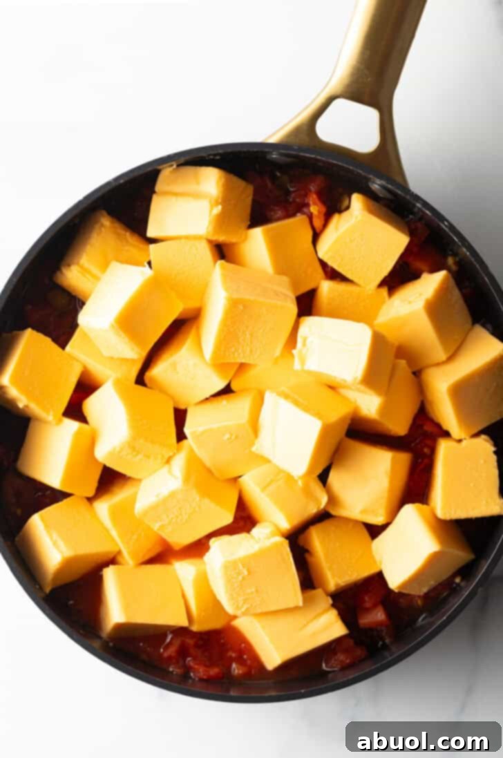 Cubes of Velveeta cheese ready to be melted in a deep black skillet, showcasing the preparation stage.