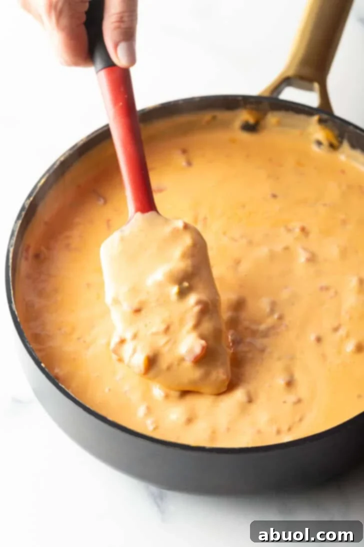 A red spatula actively stirring the melting Velveeta cheese and Rotel dip in a deep black skillet, illustrating the cooking process.