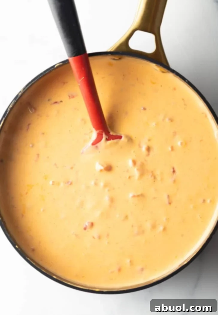 A red spatula mixing the rich Velveeta cheese and Rotel dip in a deep black skillet, capturing the creamy texture during cooking.