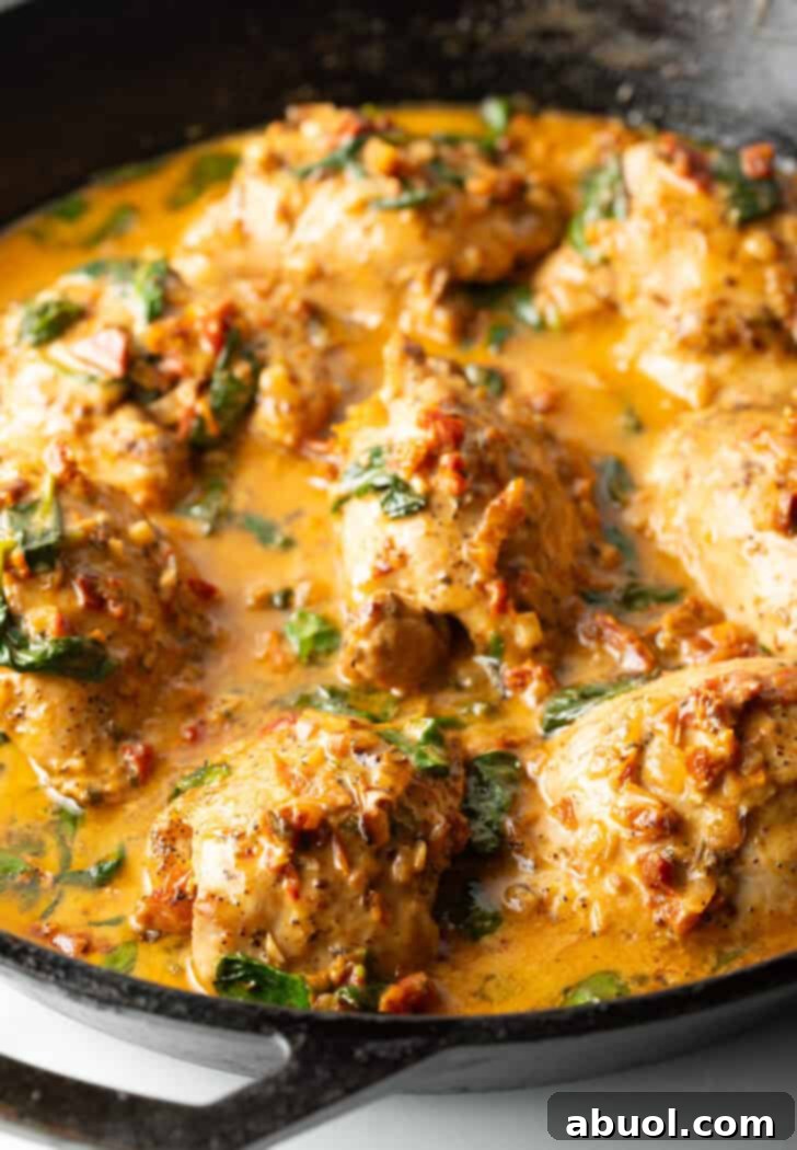 Tuscan Cream Chicken Delights 2 Creamy Tuscan chicken thighs in a skillet, bathed in a rich, red-hued sauce with spinach and sun-dried tomatoes.