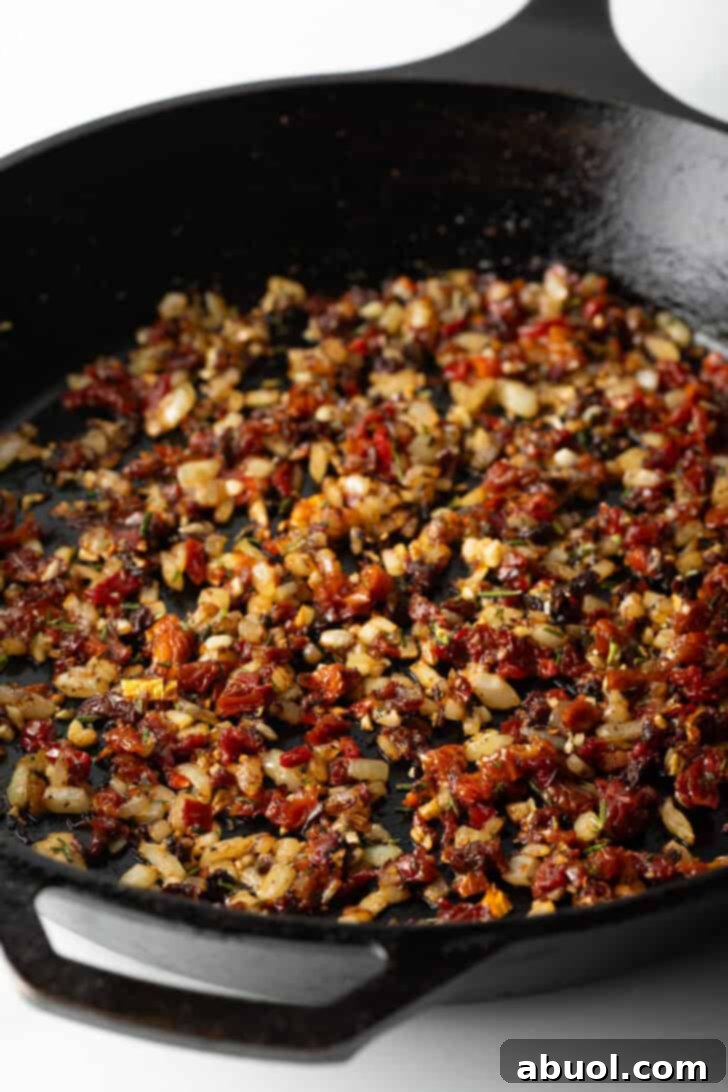 Tuscan Cream Chicken Delights 7 Cooking sun-dried tomatoes, minced garlic, and diced onion in a cast iron skillet.