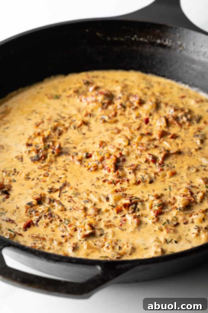 Tuscan Cream Chicken Delights 8 A cast iron skillet containing a creamy, red-hued sauce, simmering gently.