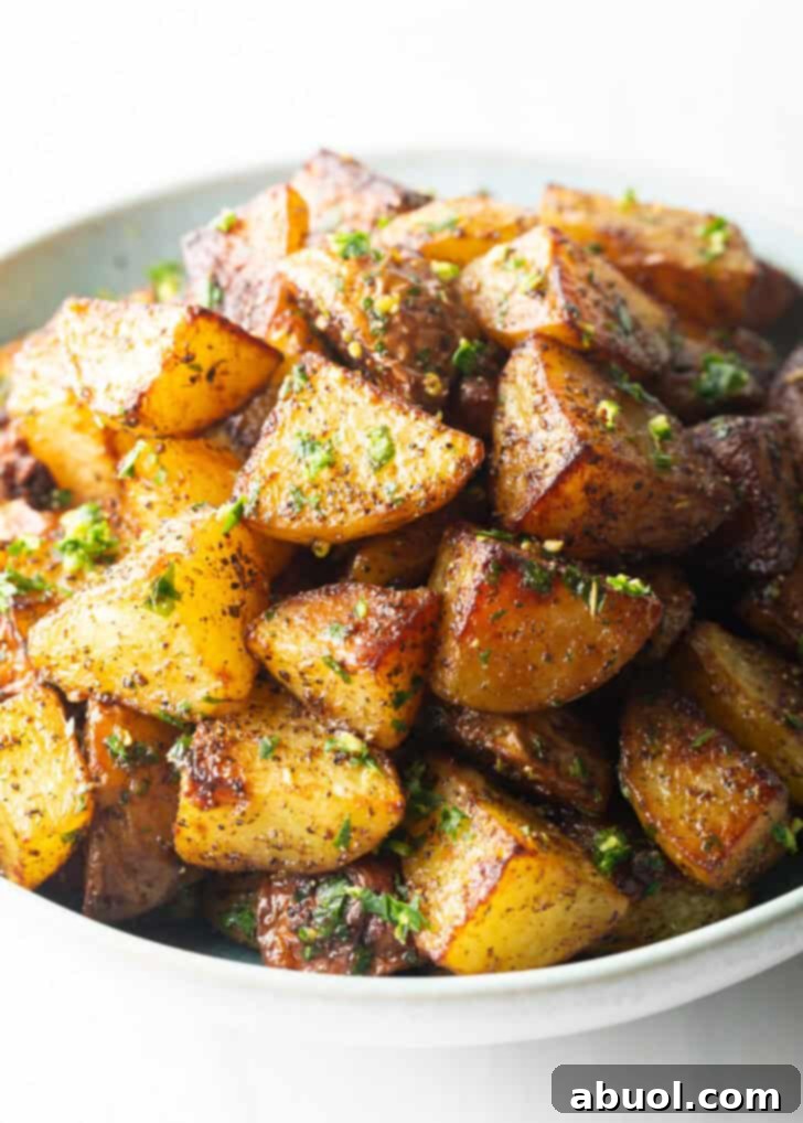 A pristine white bowl filled to the brim with perfectly golden and crispy chunks of roasted Yukon potatoes, ready to be served.