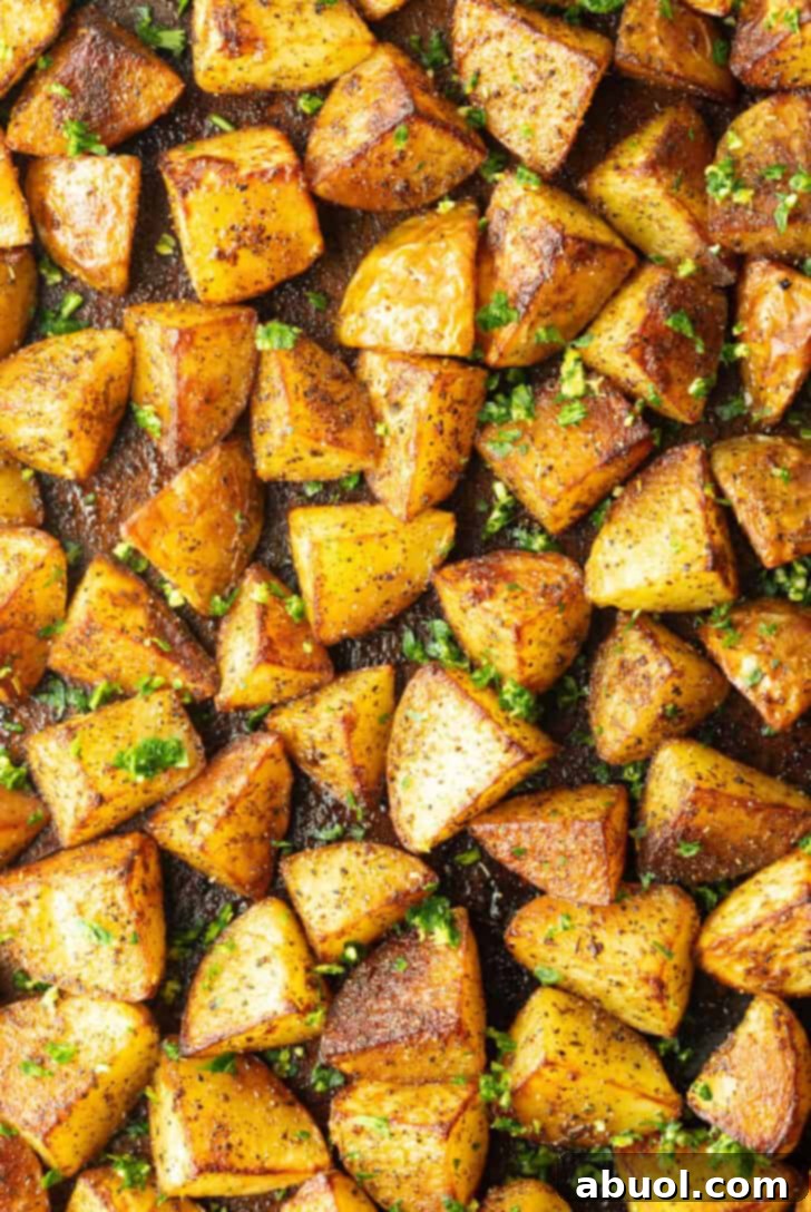 A top-down view of a large rimmed baking sheet abundantly covered with perfectly roasted, crispy golden potato chunks, glistening and ready to serve.