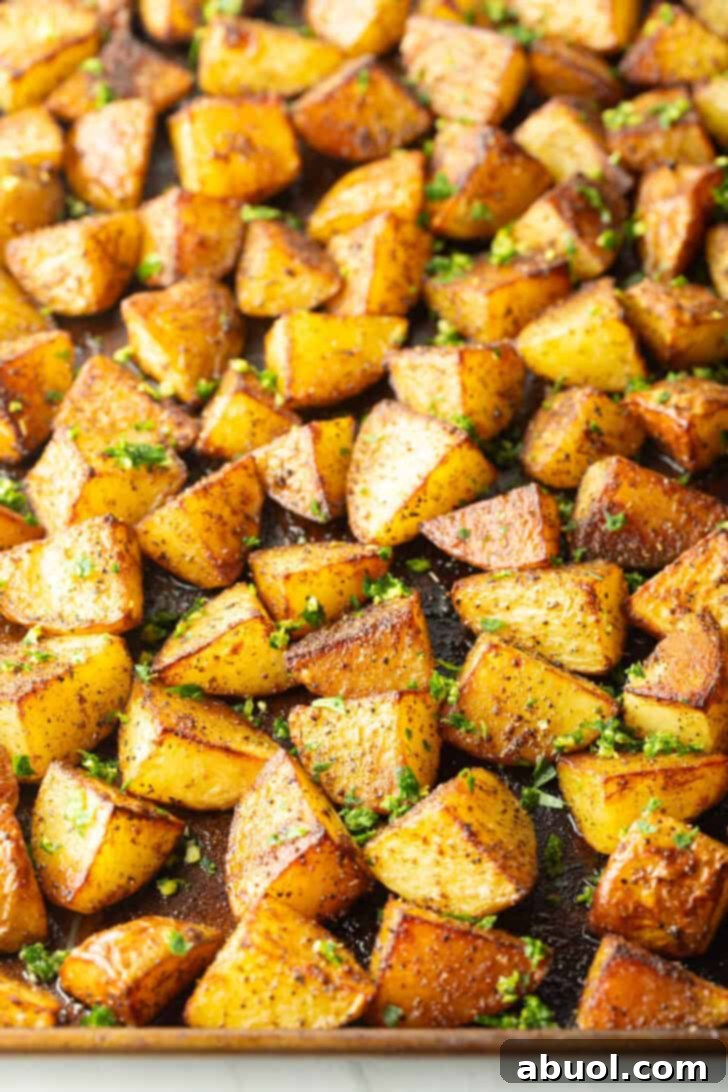 A pristine white bowl filled to the brim with perfectly golden and crispy chunks of roasted Yukon potatoes, adorned with a sprinkling of fresh green gremolata.