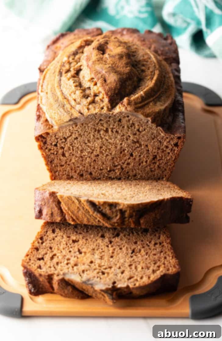 A perfectly golden loaf of healthy banana bread on a rustic cutting board, with two inviting front slices layered and ready to enjoy.