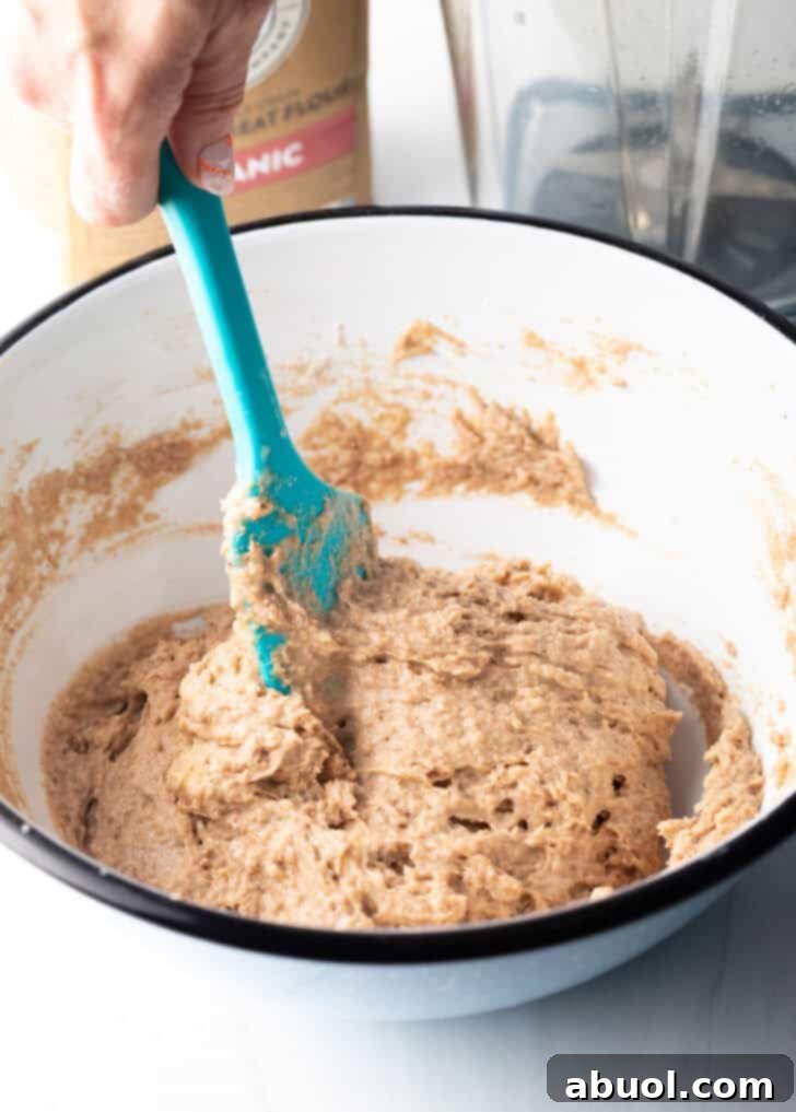 Gently stirring the banana bread batter with a blue spatula in a white mixing bowl until just combined.
