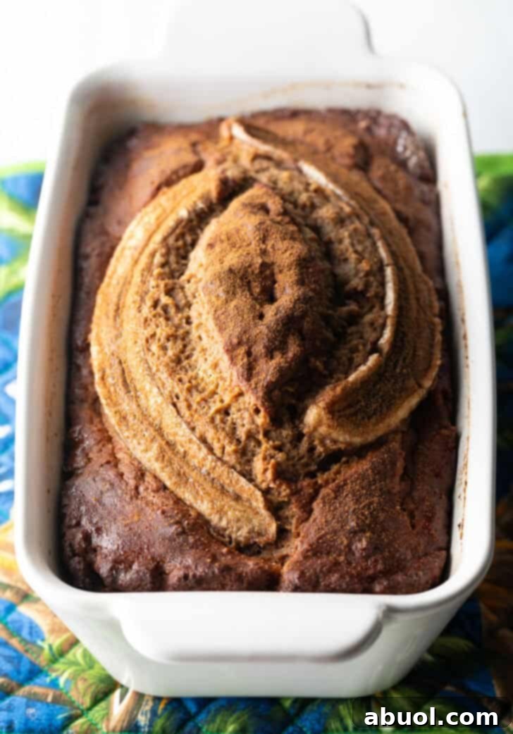 A perfectly baked, golden-brown healthy banana bread cooling in a white loaf pan after coming out of the oven.