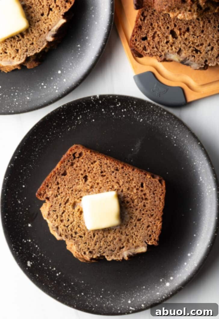 A thick, luscious slice of healthy banana bread, perfectly browned and topped with a generous pat of butter, all resting on a chic black plate.