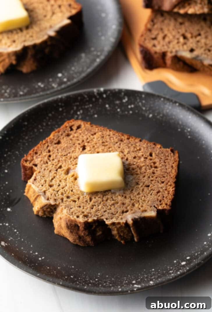 A thick, inviting slice of healthy banana bread, perfectly golden and topped with a melting pat of butter, resting on a sleek black plate.