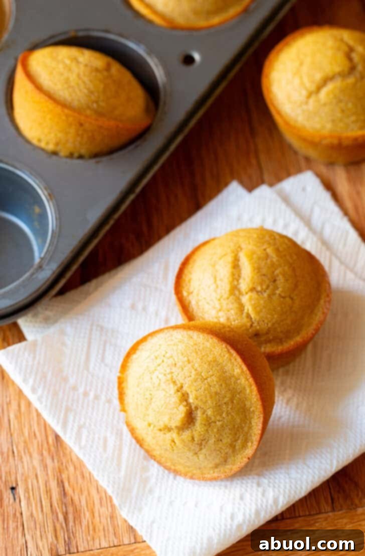 Two honey cornbread muffins on a white napkin, next to a muffin baking tin with more muffins.
