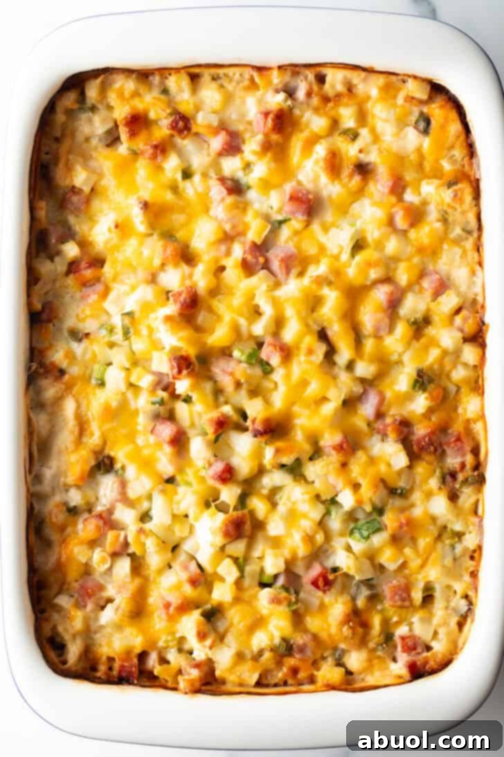 Top down view of the entire cheesy ham and potato casserole in a white baking dish on a wooden surface.