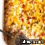 Top down view white casserole dish with ham and potatoes, and a spoon in the dish where a serving has been removed.