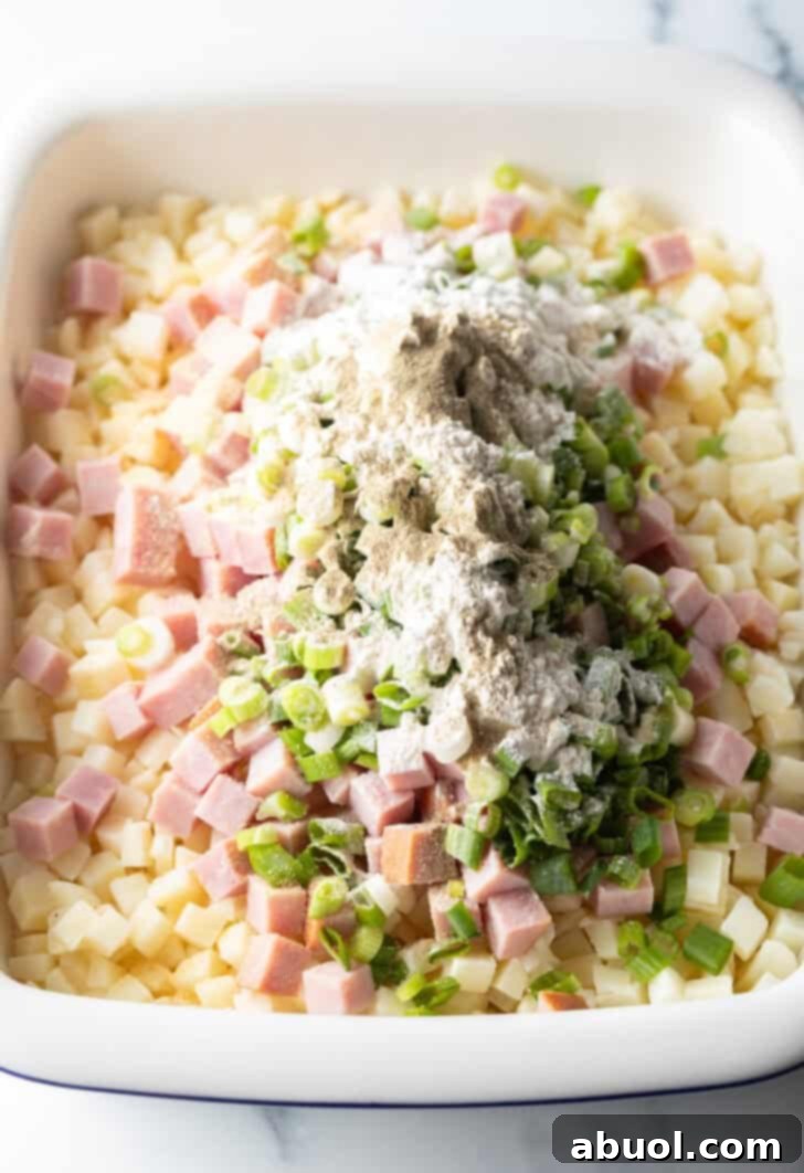 Mixing potatoes, ham, green onions, garlic, and flour in a baking dish.