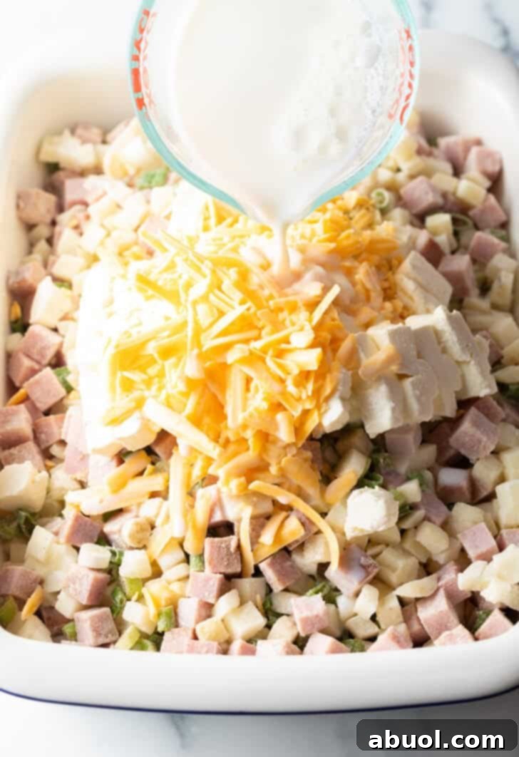 Adding milk to the chopped potatoes, ham, and shredded cheese in a casserole dish.