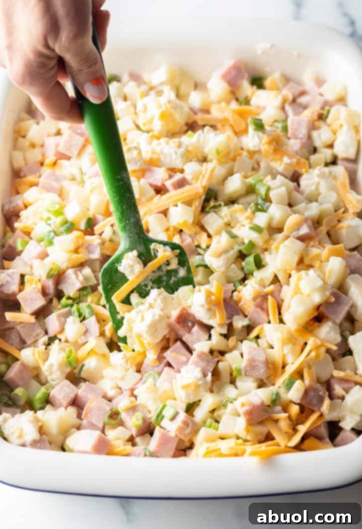 Gently stirring the casserole ingredients to combine cream cheese and shredded cheese evenly.