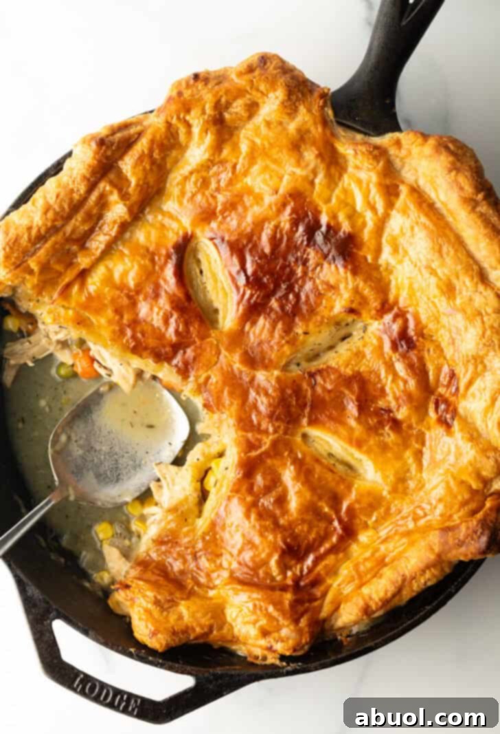 Skillet of chicken pot pie topped with golden brown puff pastry. A serving spoon has removed a quarter portion.