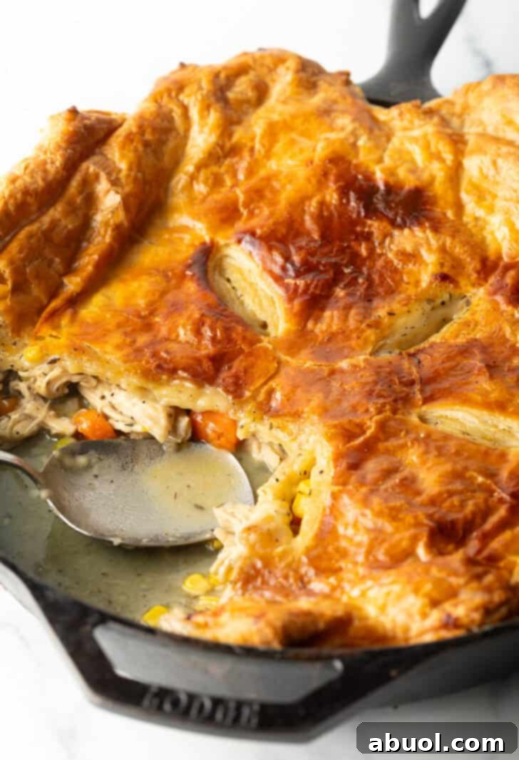 Skillet of chicken pot pie topped with golden brown puff pastry. A serving spoon has removed a quarter portion.
