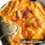 Skillet of chicken pot pie topped with golden brown puff pastry. A serving spoon has removed a quarter portion.