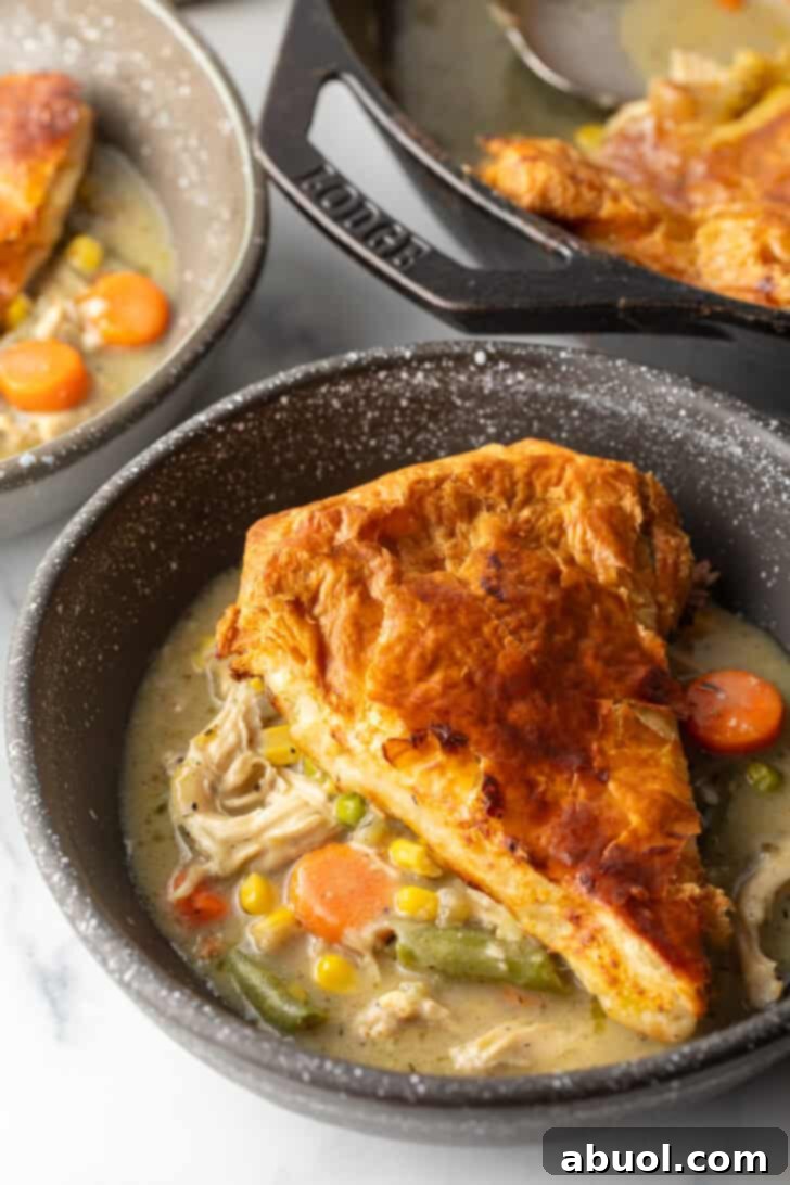 Top down view of a wedge of chicken pot pie with puff pastry crust on a black plate.