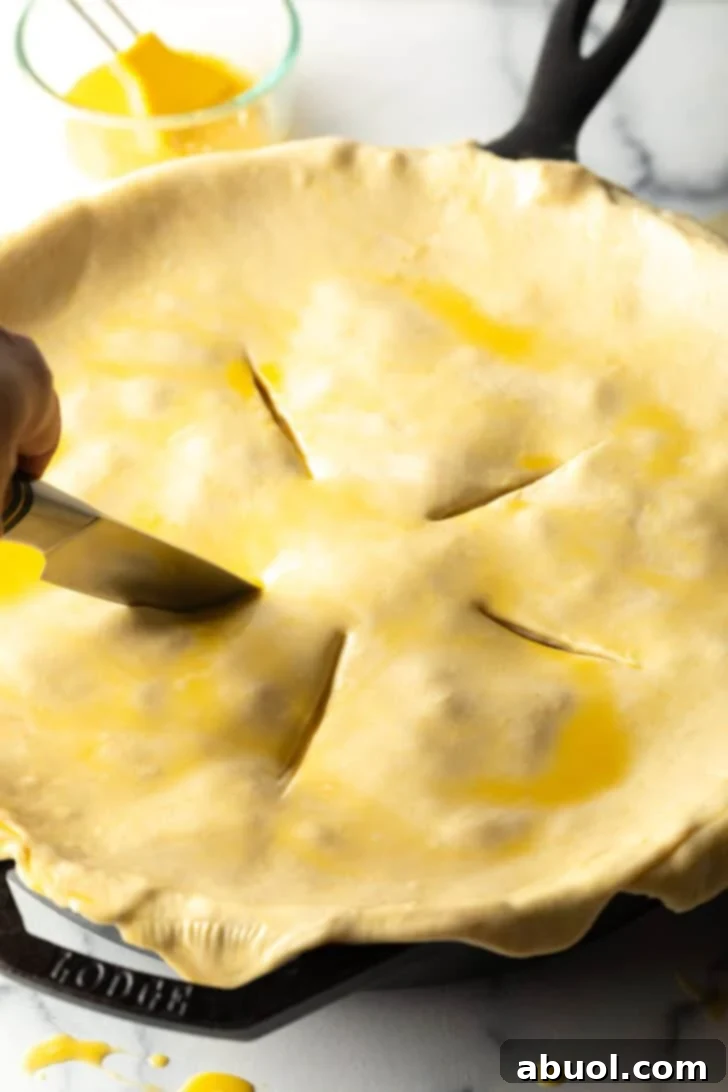 Pie crust being prepped for baking with a knife cutting slits in the top.