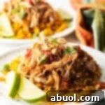 Mound of zesty shredded Mexican chicken on a plate with Spanish rice and lime wedges.