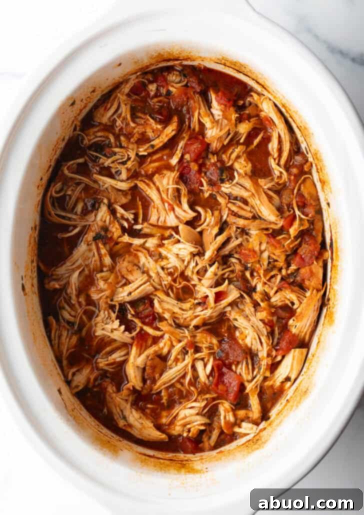 Top down view of seasoned shredded Mexican chicken simmering in a crockpot, illustrating the slow cooking process.