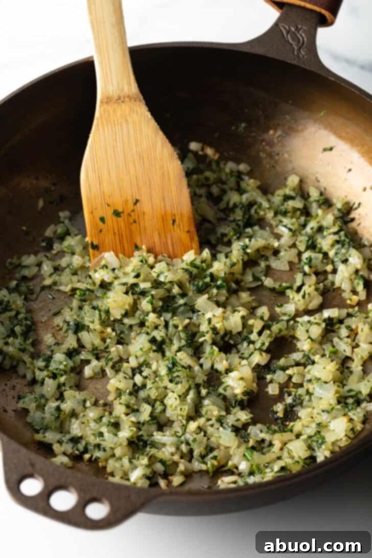 Using a wooden spatula to cook onions and seasonings in a large cast iron pan, demonstrating the initial sauté step.