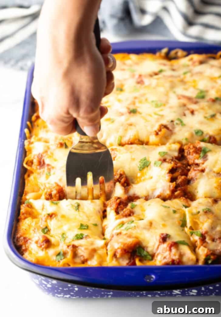 Using a metal spatula to cut the baked spaghetti casserole into 12 even pieces, ready for serving.