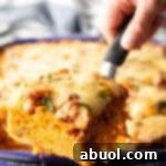 Hand with a spatula holding a serving of baked spaghetti casserole, highlighting the savory meat sauce and melty cheese.