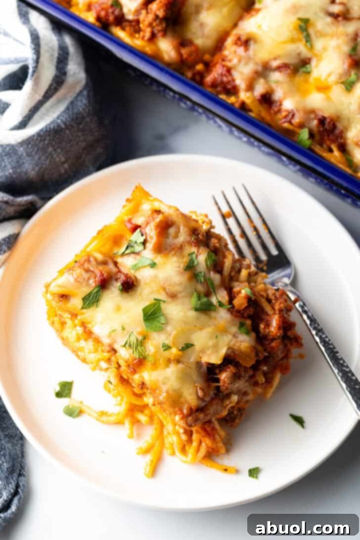 Top down view of a white plate with a serving of baked spaghetti casserole and fork, showing layers of pasta, sauce, and cheese.
