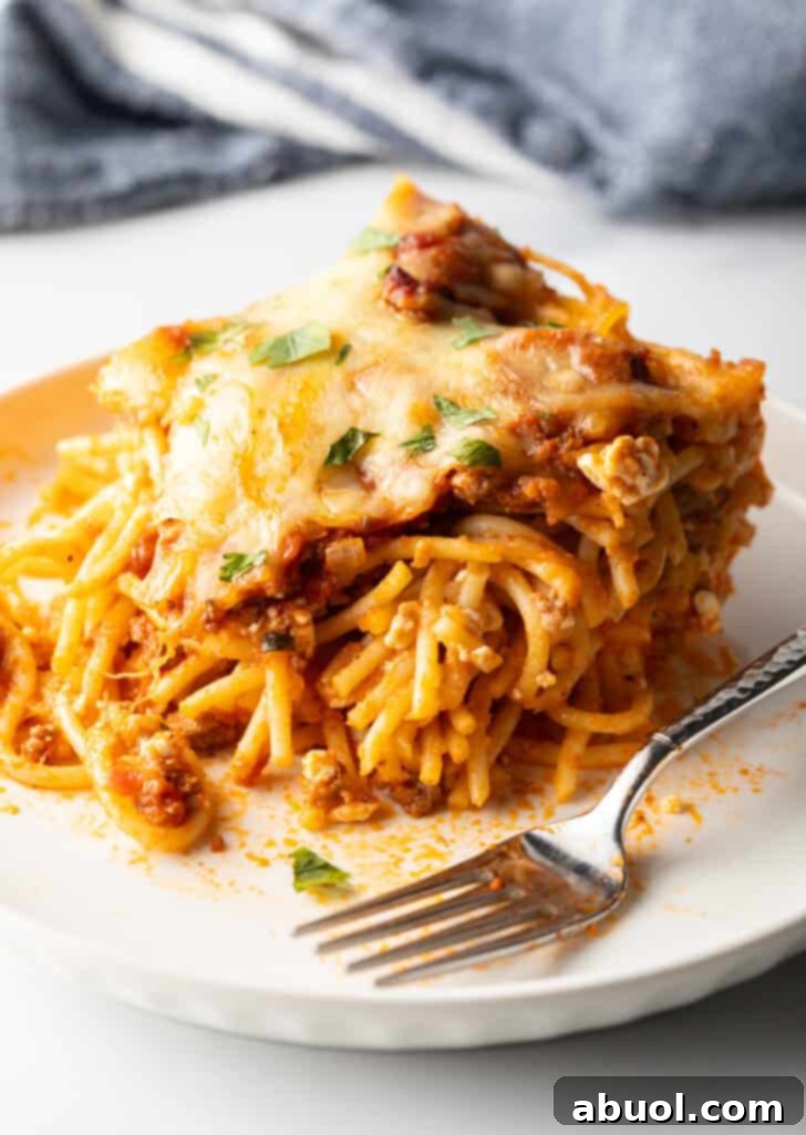 White plate with a generous serving of spaghetti bake and a fork, highlighting the melty cheese and hearty sauce.