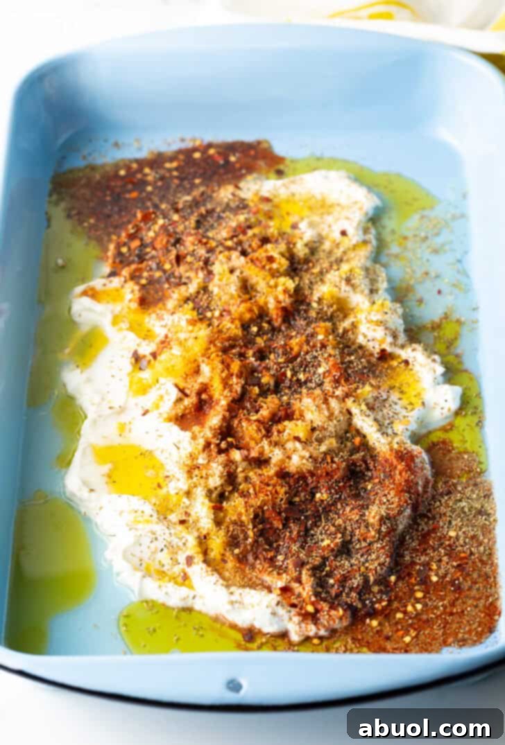 Combination of yogurt, olive oil, and Greek spices in a blue rectangular baking dish, ready for chicken.
