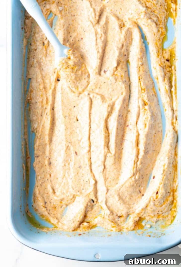 Top down view of a blue spatula spreading yogurt marinade in the bottom of a blue rectangular baking dish.