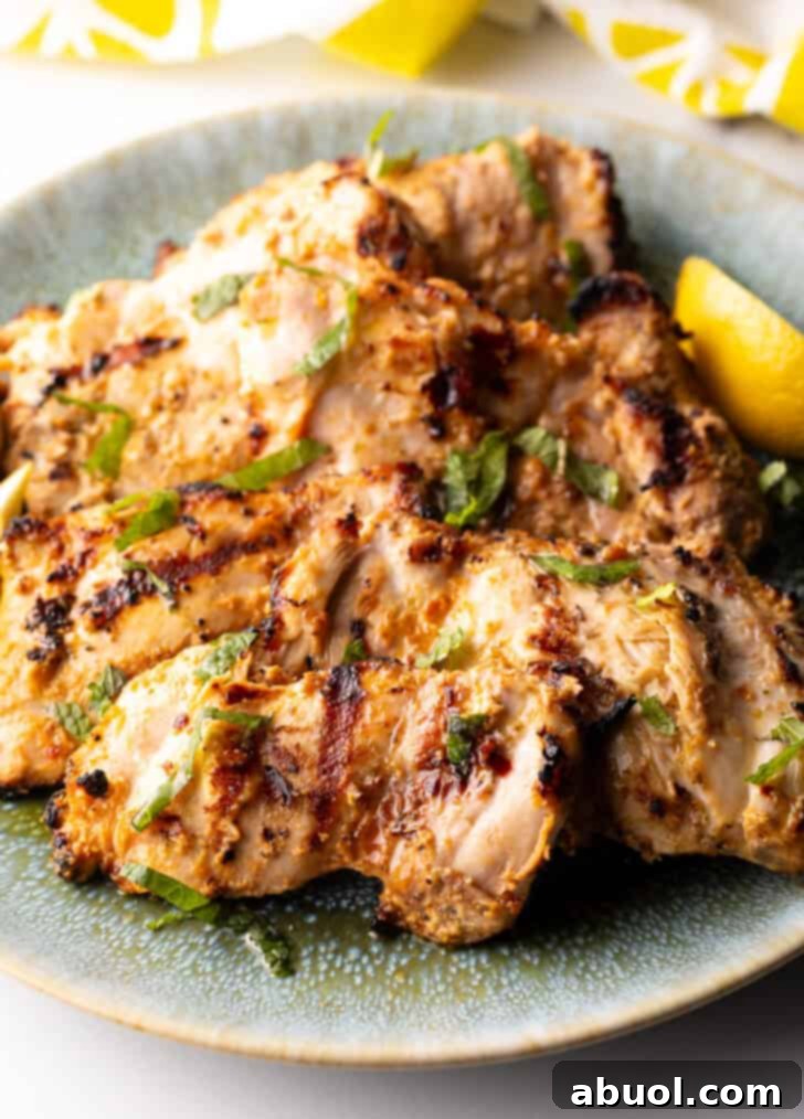 Grilled marinated chicken thighs in a shallow blue bowl, garnished with fresh herbs and lemon wedges.