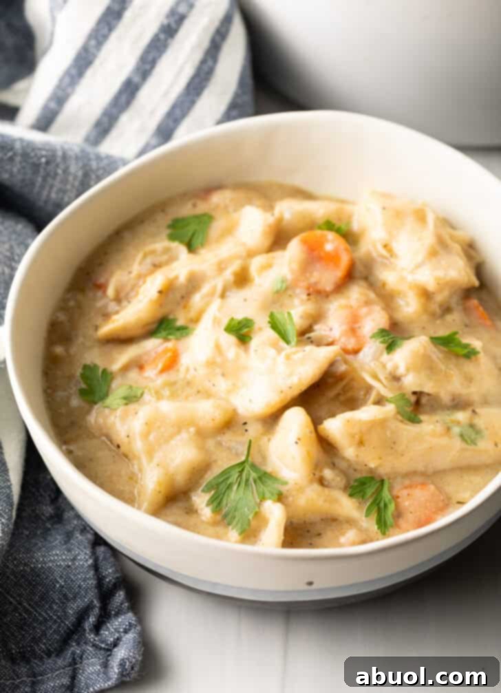 White bowl with crock pot chicken and dumplings sprinkled with fresh chopped parsley.