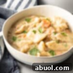 White bowl with crock pot chicken and dumplings sprinkled with fresh chopped parsley.