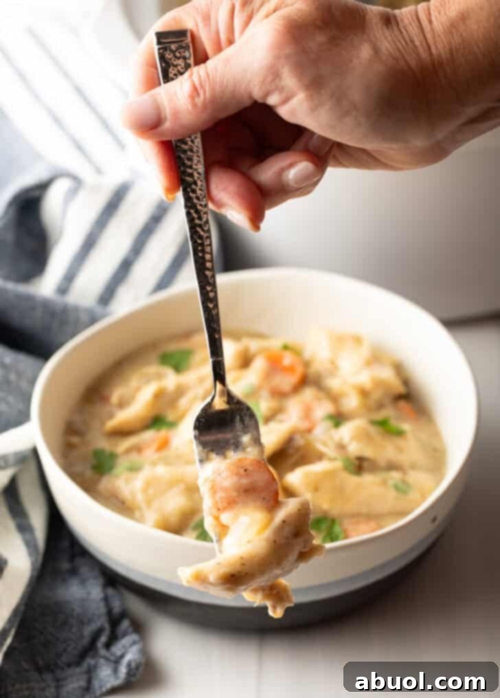 Hand holding a forkful of chicken in dumplings to camera.