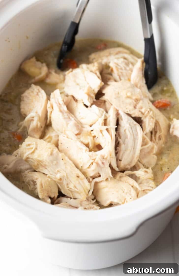 Tongs grabbing shredded chicken from a white crockpot.