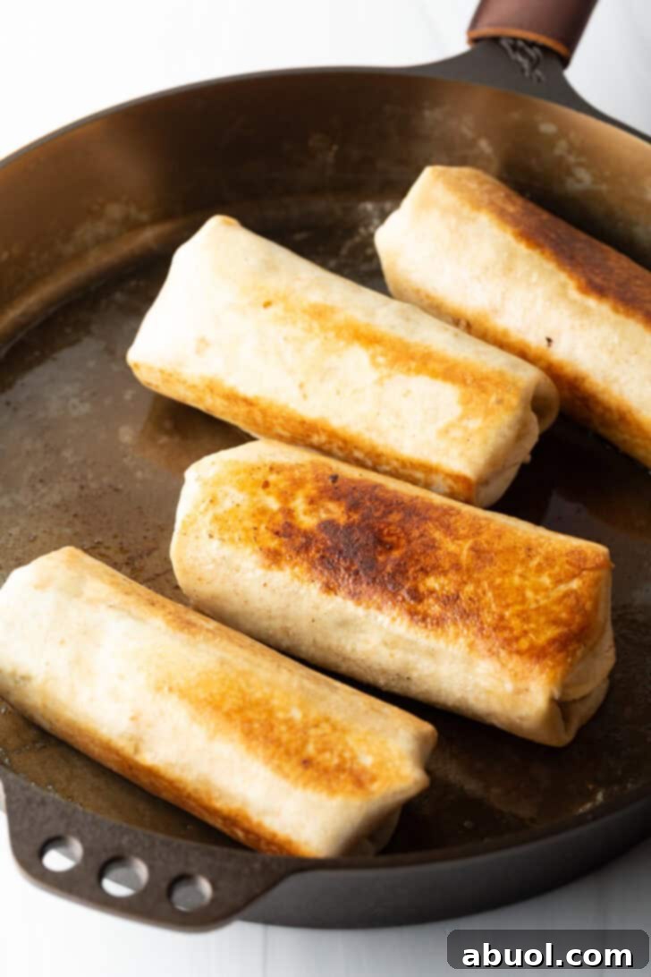Four seared burritos on a large pan.