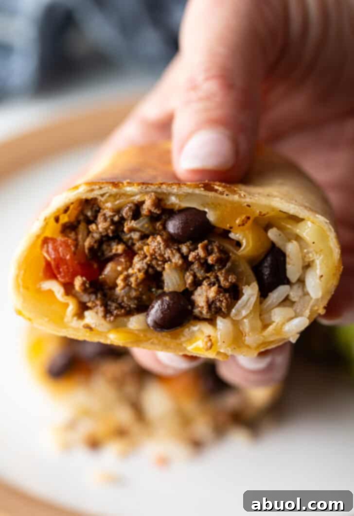 Hand holding the cut side of a beef burrito to camera.