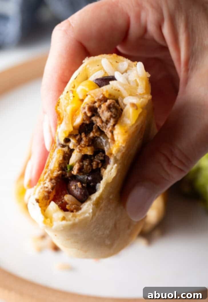 Hand holding the cut side of a beef burrito to camera.