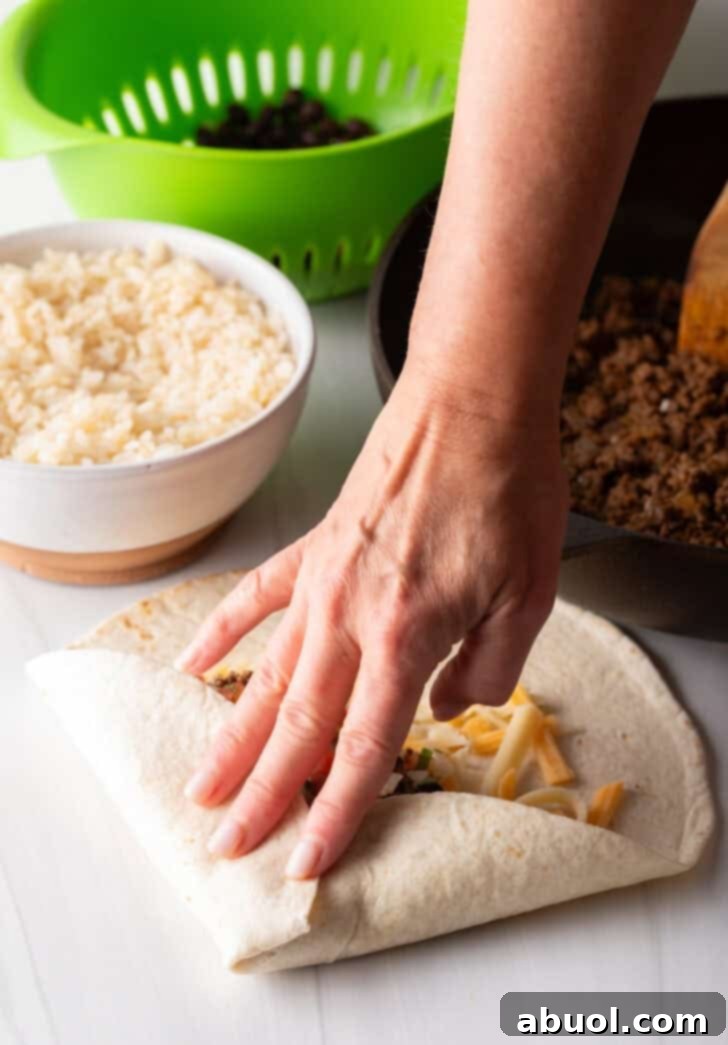 Hand folding a tortilla to make a burrito filled with beef and cheese.
