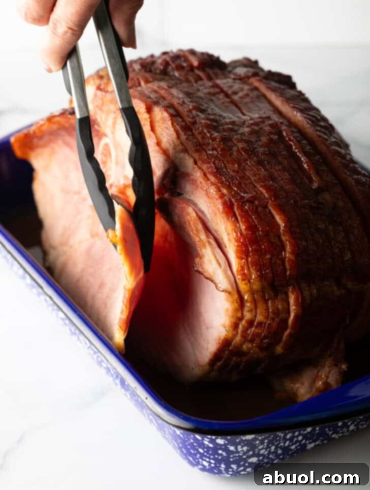 Tongs gracefully removing the first tender slice of a perfectly cooked and glazed spiral ham from a baking dish, showcasing its juicy interior.
