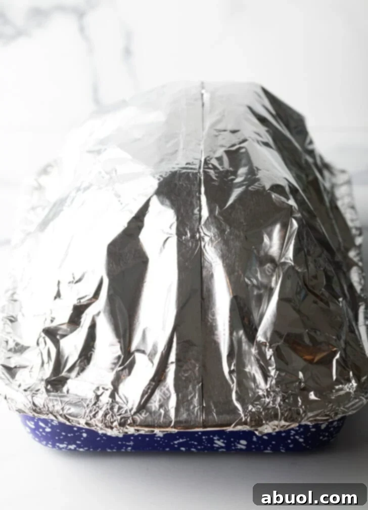 Spiral ham in a roasting pan, completely sealed with aluminum foil.