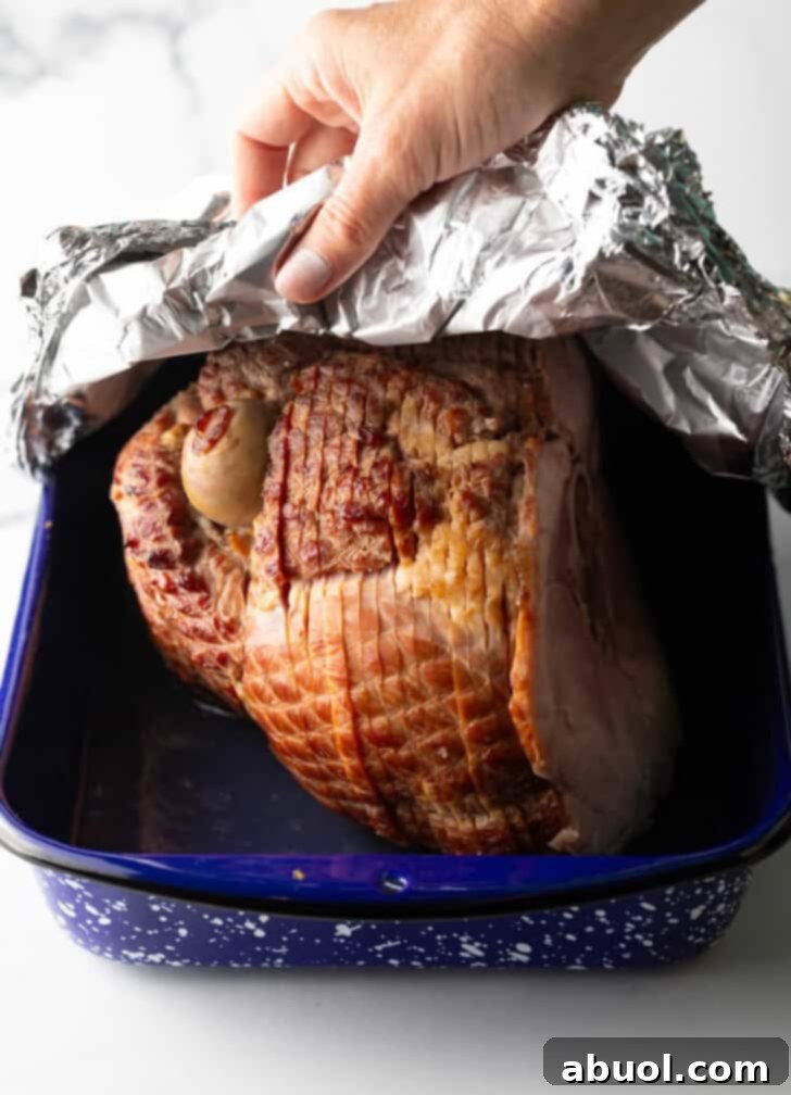 Applying aluminum foil tightly over a spiral ham in a blue and white speckled roasting pan.