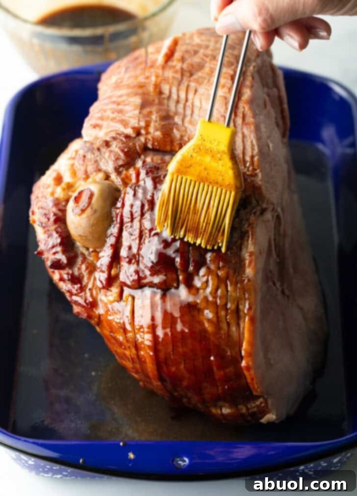 Basting a cooked spiral ham with a delicious glaze using a yellow silicone brush, ensuring even coating.